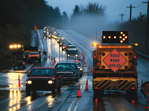 rainy road work zone with attenuator truck and lane closed arrow