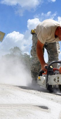 worker cutting concrete with a power saw in a cloud of dust