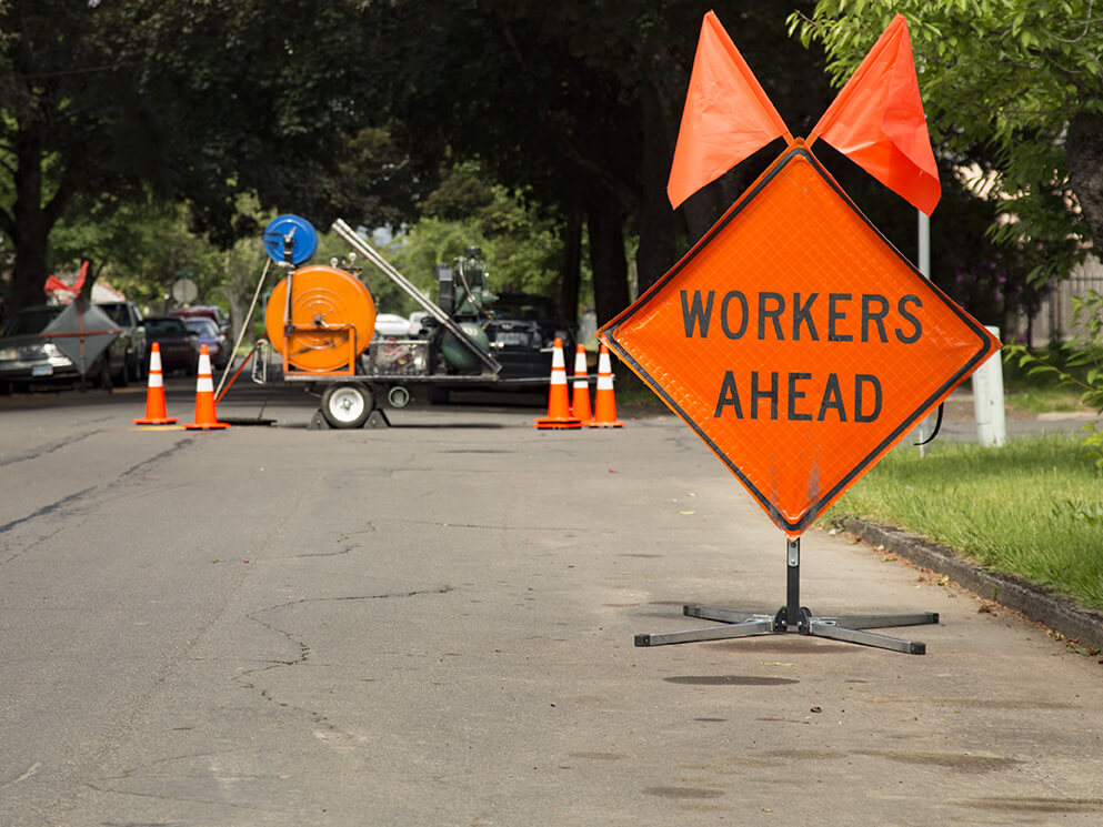 orange diamond ‘workers ahead’ warning sign posted before a road repair project