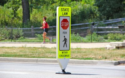 an in-street stop-for-pedestrians sign with runner in the background