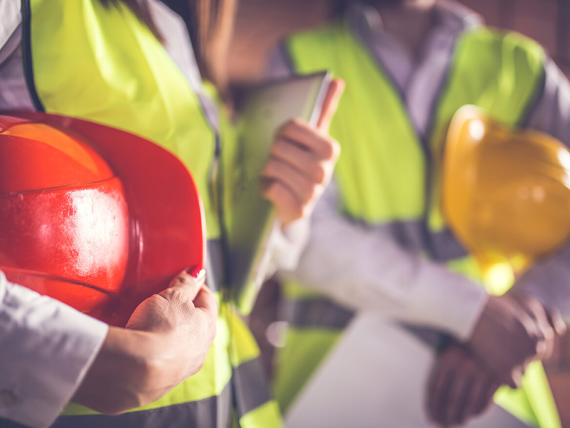 tightly cropped image of transportation workers with hardhats and schematicis