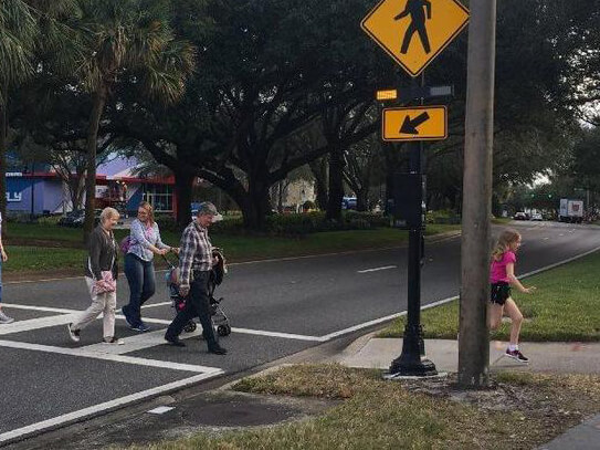 pedestrians in a crosswalk that is marked with a flashing beacon