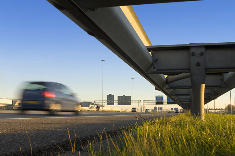 low view of roadside guard rail, grass, and car speeding by